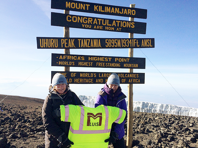 Two women at the summit of Mt. Kilimanjaro, Africa, standing in front of the sign at the peak.