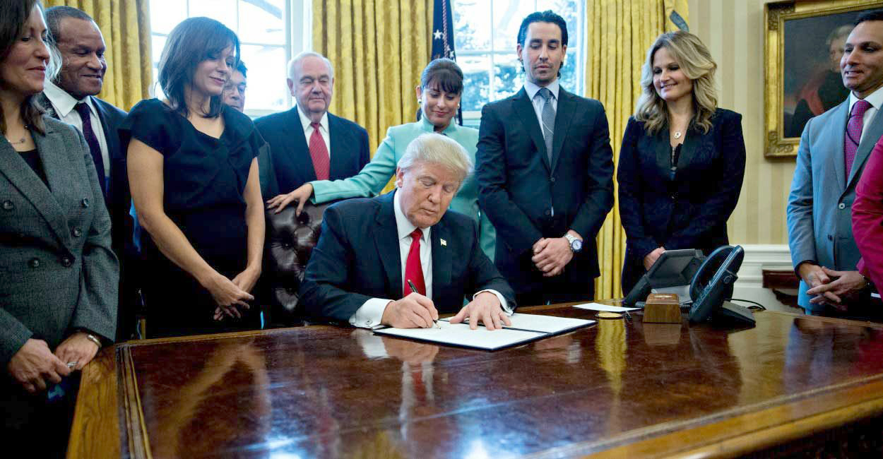 President Trump signing the 2017 Tax Cuts and Jobs Act into law with people watching him